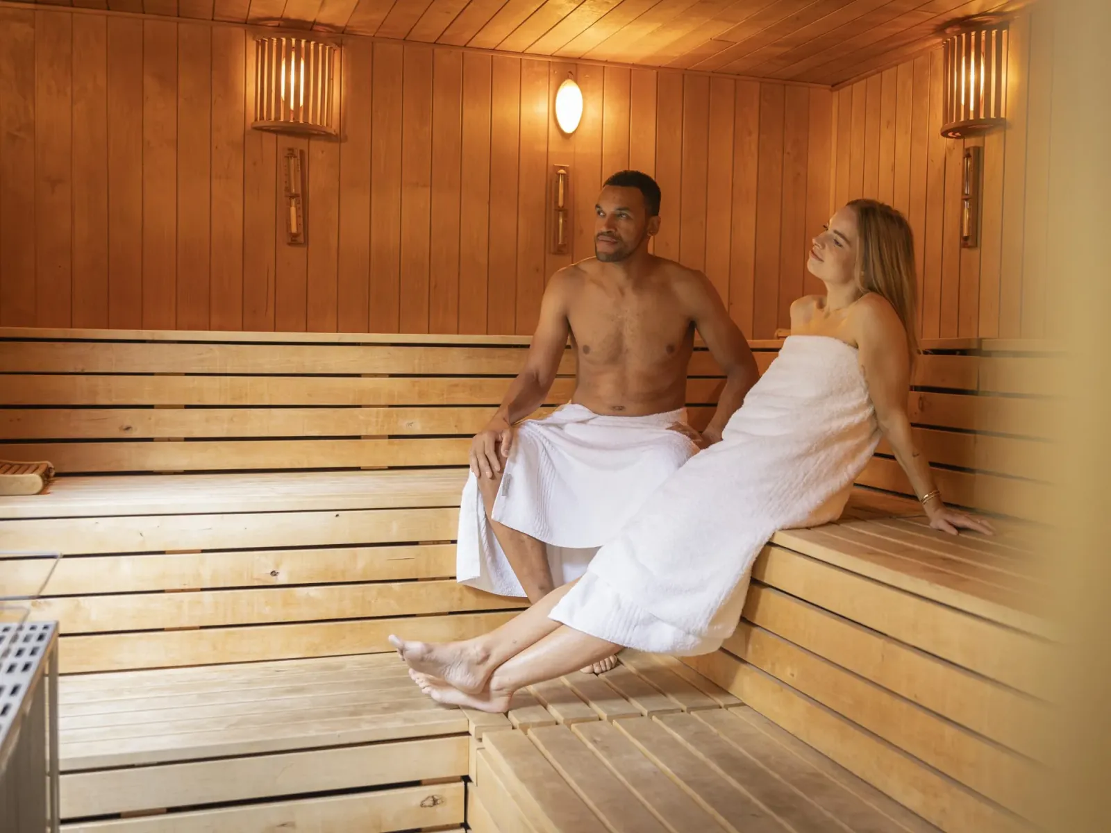 Ein Mann und eine Frau sitzen in Handtüchern auf den Holzbänken der Sauna